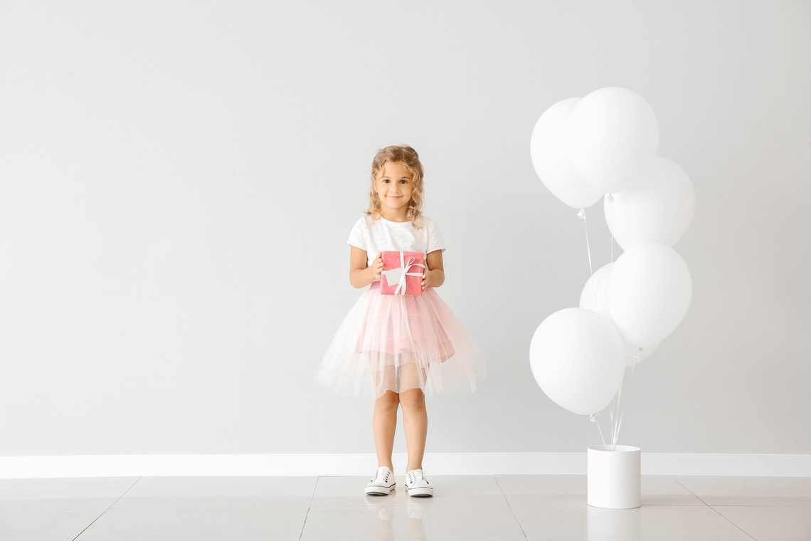 Little Girl with Balloons and Gift near Light Wall